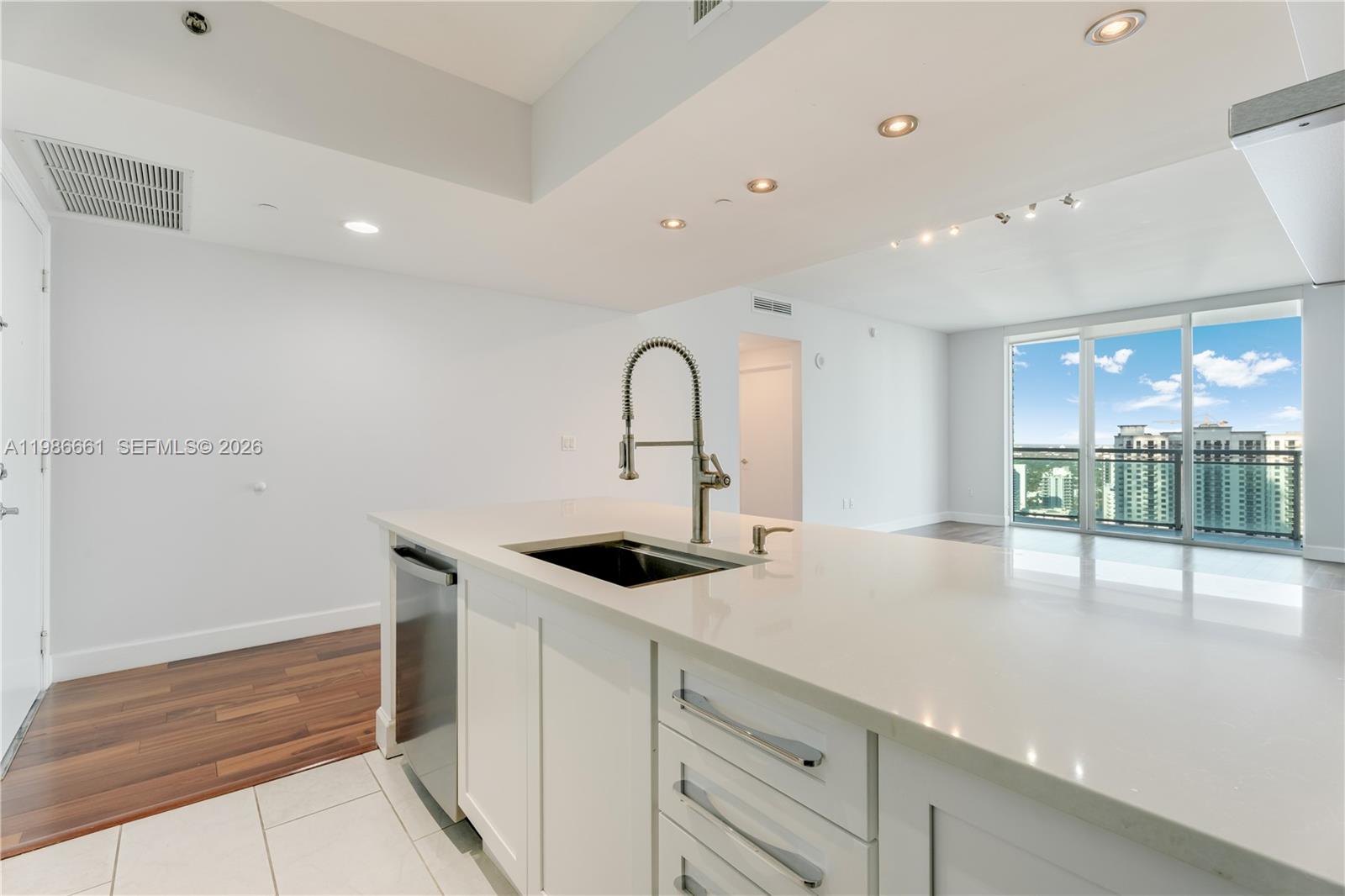A modern kitchen island with a sink and stainless steel dishwasher faces a bright living area — 951 Brickell Ave # 3607, Miami FL 33131, MIAMI, FL