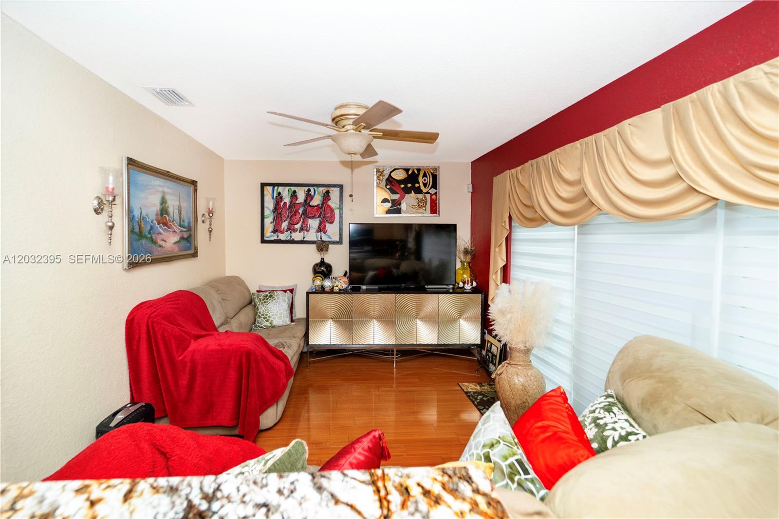 A living room features a television on a gold cabinet, two sofas, and red accents — 8564 SW 23rd Ct, Miramar FL 33025, MIRAMAR, FL