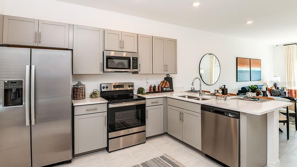 A modern kitchen features gray cabinets, stainless steel appliances, and a white quartz countertop island — 10645 ORBIT TERRACE, SARASOTA, FL