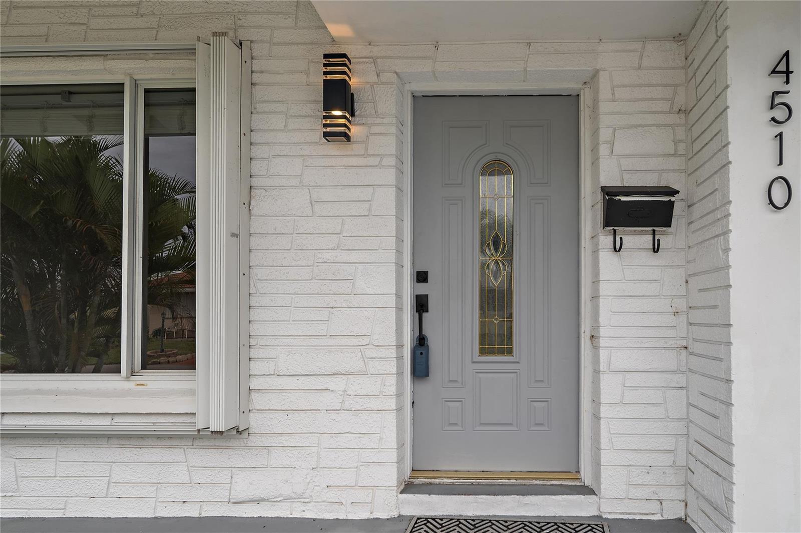 A gray front door with a glass insert sits beside a window and house numbers — 4510 NW 49th Drive, Tamarac FL 33319, TAMARAC, FL