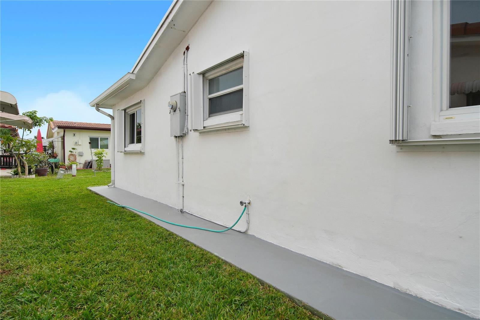 The exterior side of a white house features a grey concrete walkway and green lawn — 4510 NW 49th Drive, Tamarac FL 33319, TAMARAC, FL