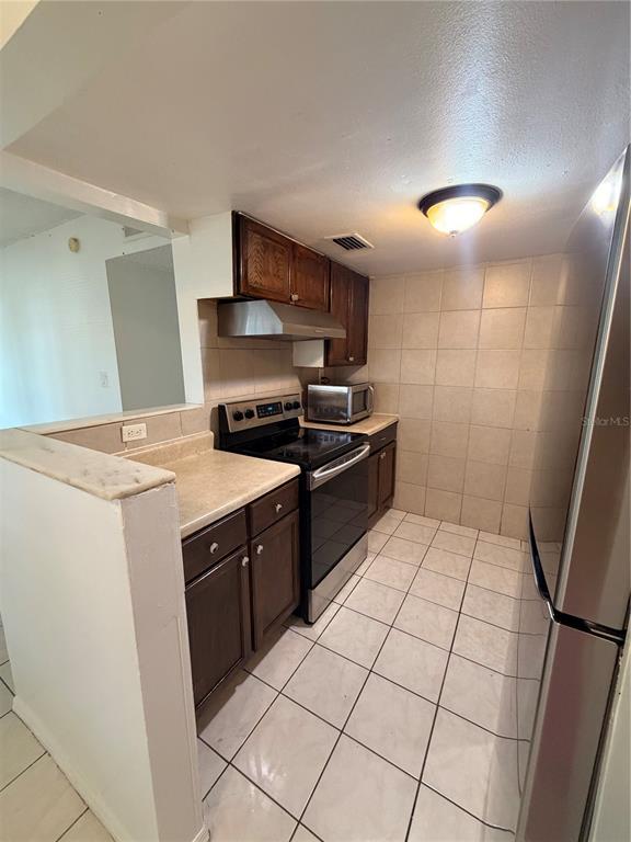 A kitchen features dark wood cabinets, stainless steel appliances, and light-colored tile flooring — 1432 HOLDEN AVENUE UNIT C6, ORLANDO, FL