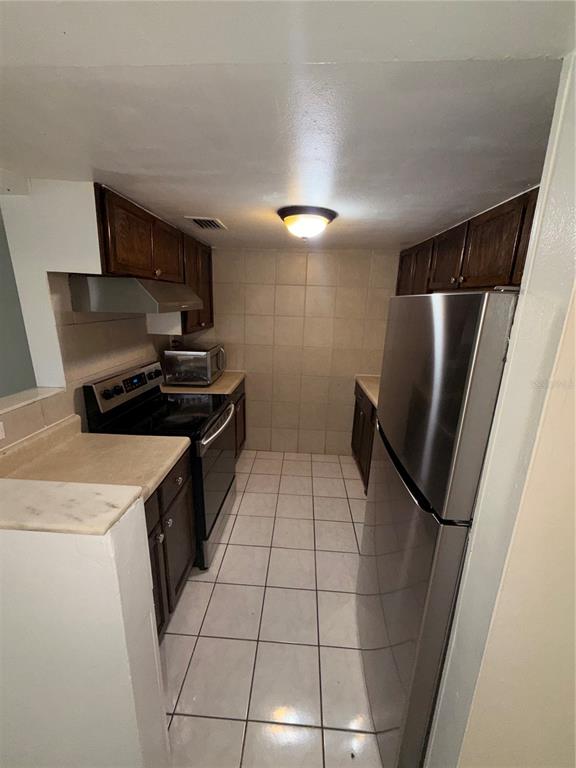 A galley kitchen features dark wood cabinets, stainless steel appliances, and light-colored tile flooring — 1432 HOLDEN AVENUE UNIT C6, ORLANDO, FL