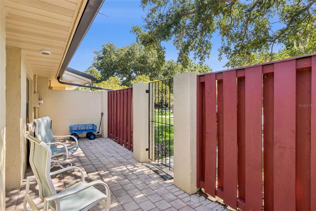A paved patio features two chairs, a small blue wagon, and a red wooden fence — 664 CLUBHOUSE ROAD, WINTER HAVEN, FL