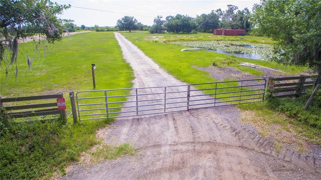A metal gate blocks a dirt driveway leading into a grassy field with a pond — 7977 BARR ROAD, MYAKKA CITY, FL