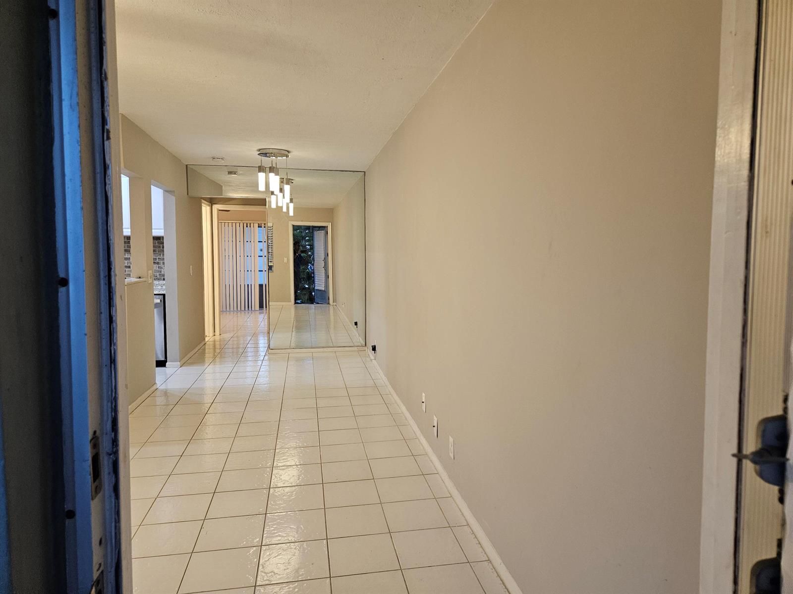 A long hallway with white tile flooring, a large wall mirror, and a modern light fixture — 71 Easthampton # C, West Palm Beach FL 33417, WEST PALM BEACH, FL