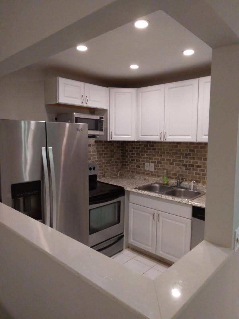 A small kitchen with white cabinets, stainless steel appliances, and a brown brick backsplash — 71 Easthampton # C, West Palm Beach FL 33417, WEST PALM BEACH, FL