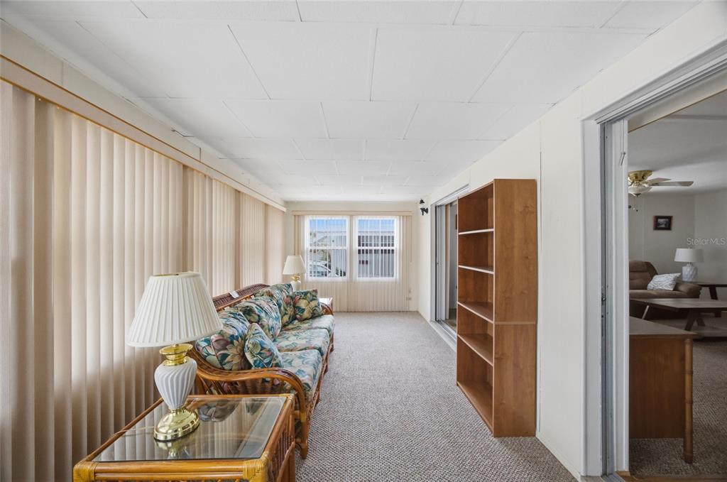 A sunroom features a floral sofa, a wooden bookshelf, and carpeted flooring — 9900 ULMERTON ROAD UNIT 242, LARGO, FL