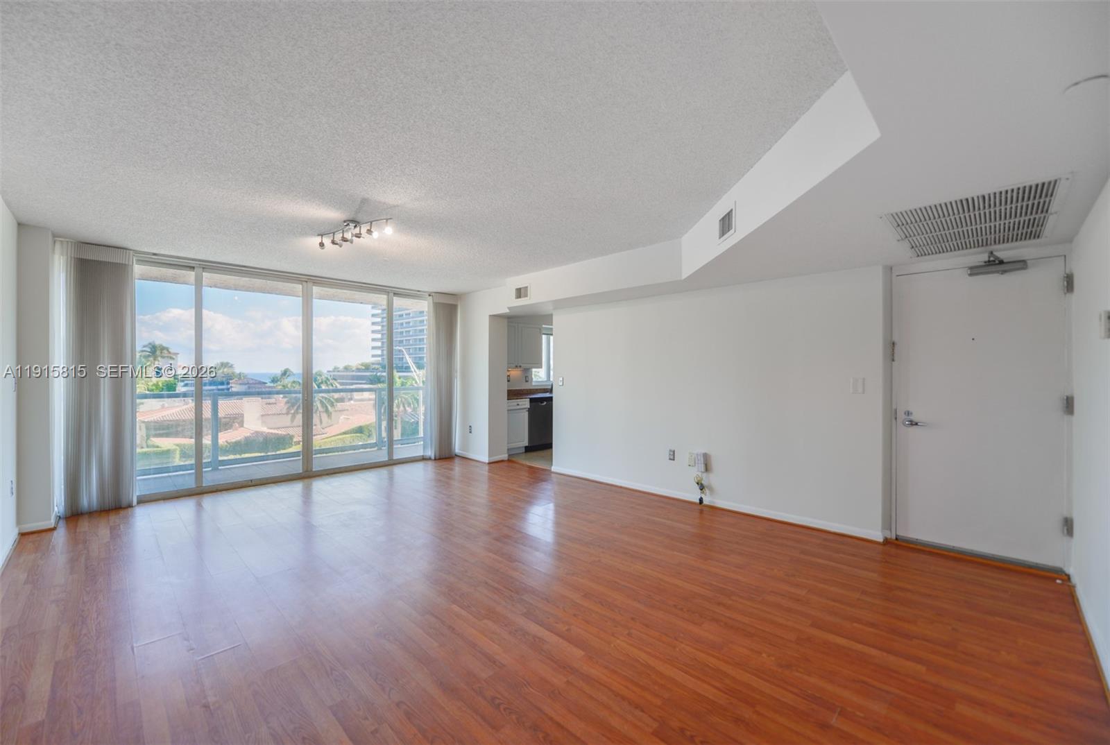 An empty living room features wood-look flooring, a ceiling light fixture, and a balcony view — 5900 Collins Ave # 506, Miami Beach FL 33140, MIAMI BEACH, FL