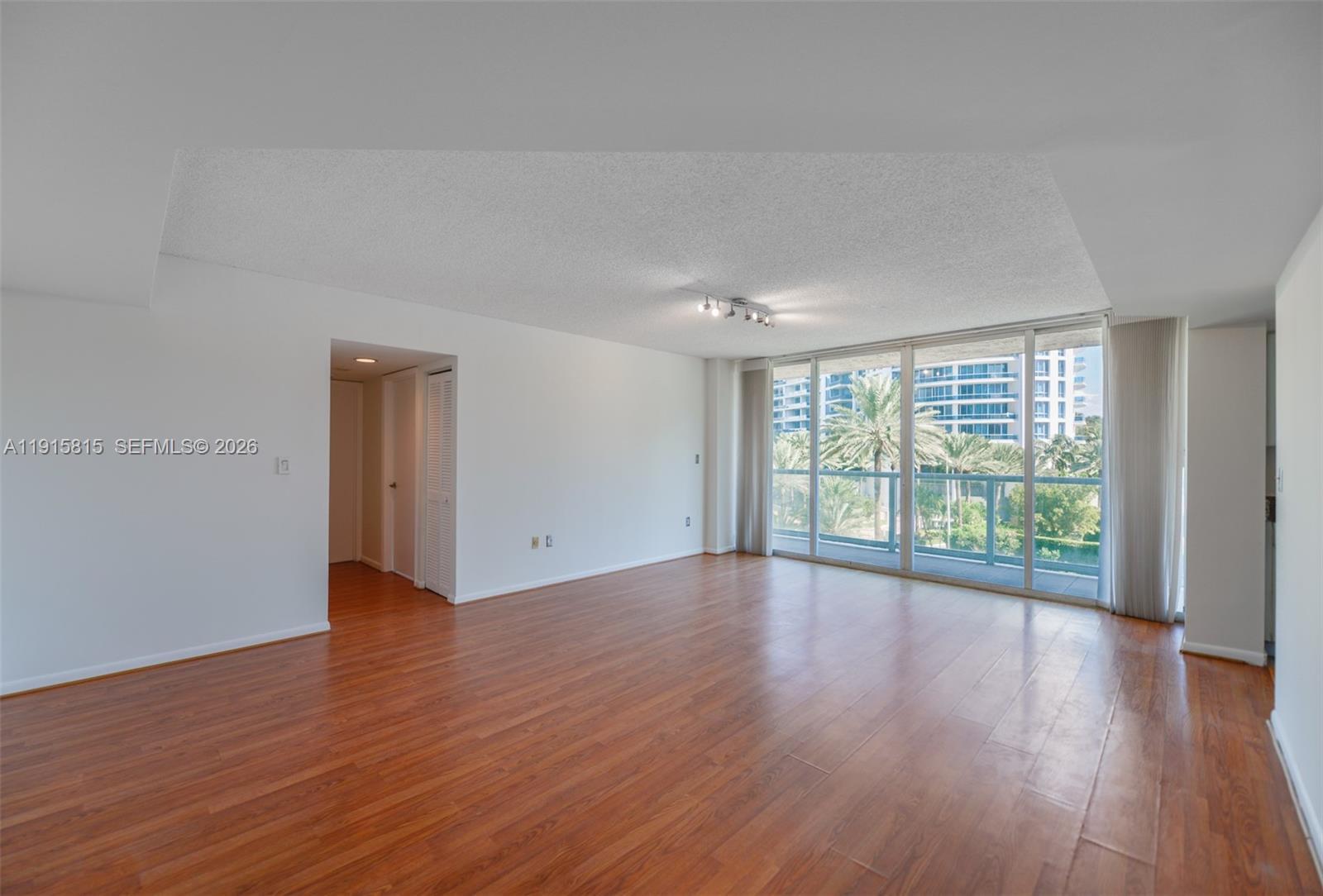 An empty living room features wood-look flooring, white walls, and floor-to-ceiling windows with balcony access — 5900 Collins Ave # 506, Miami Beach FL 33140, MIAMI BEACH, FL