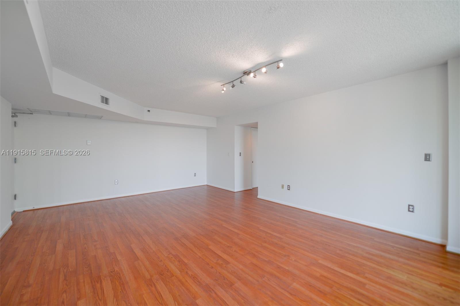 An empty room features white walls, wood-look flooring, and a track lighting fixture — 5900 Collins Ave # 506, Miami Beach FL 33140, MIAMI BEACH, FL