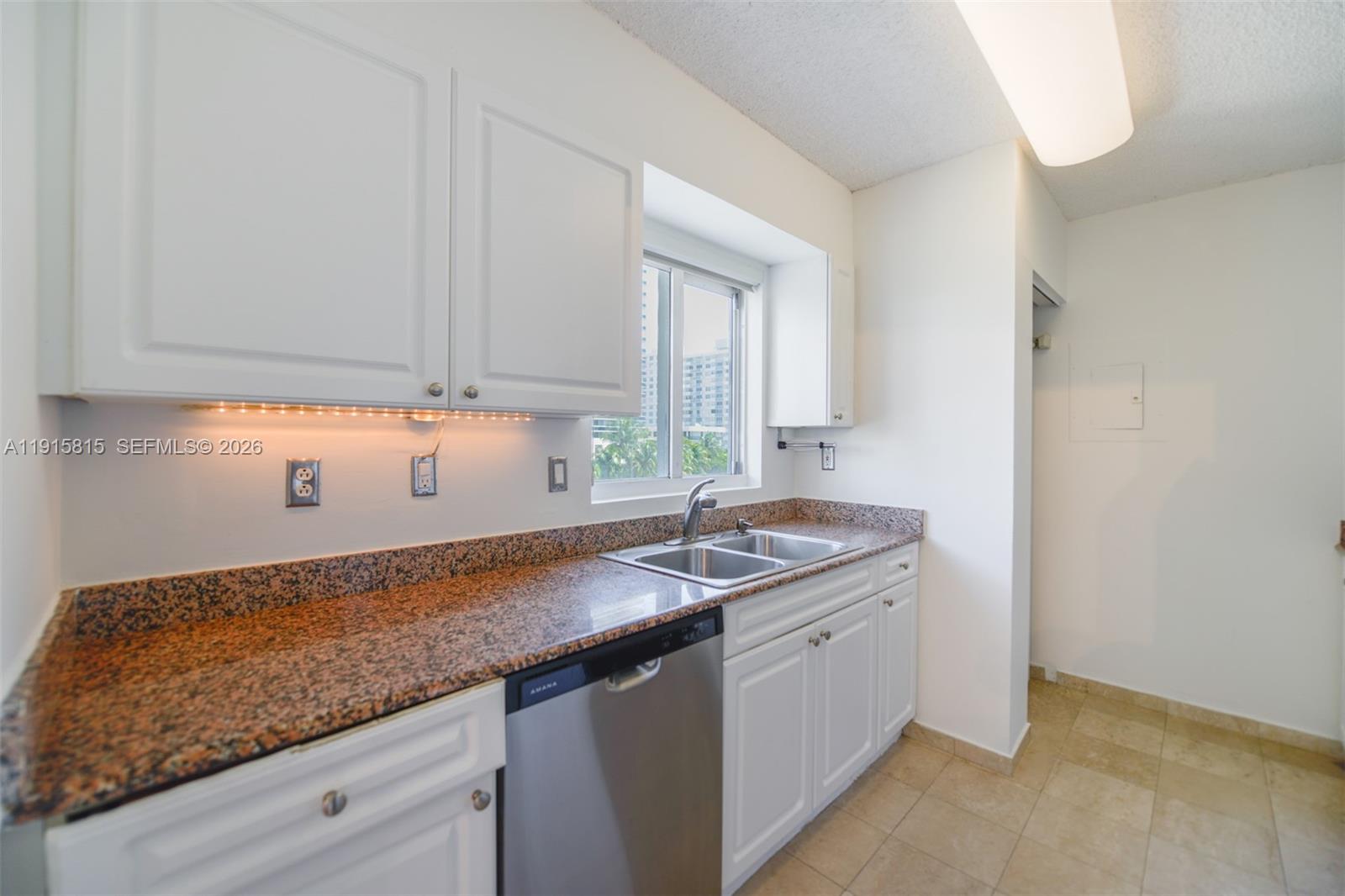 A kitchen features white cabinets, granite countertops, a stainless steel dishwasher, and a double sink — 5900 Collins Ave # 506, Miami Beach FL 33140, MIAMI BEACH, FL