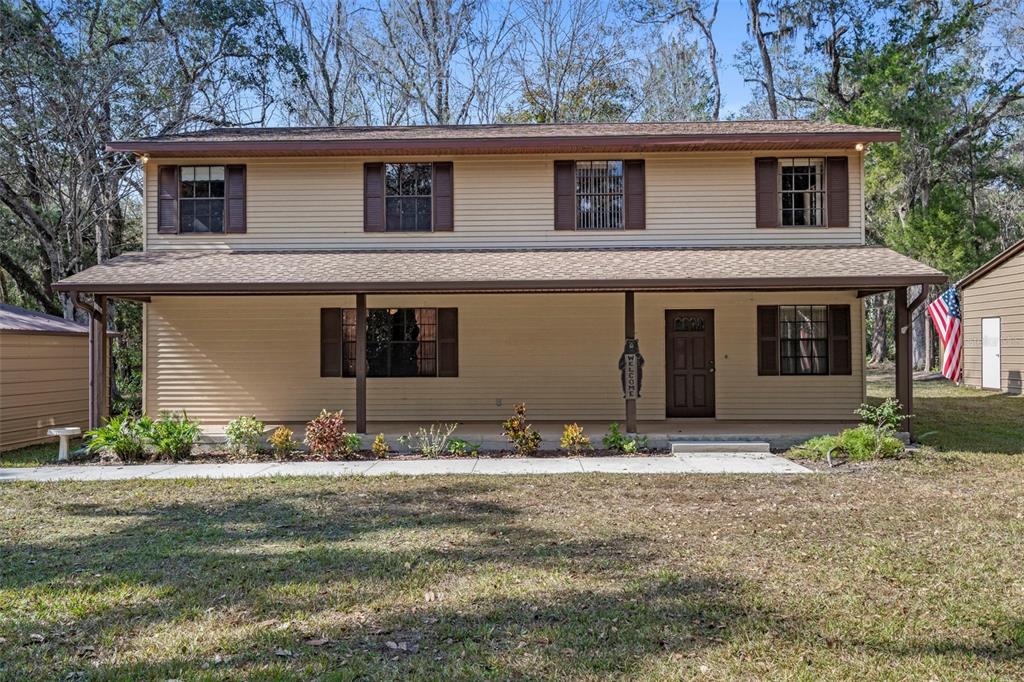 A two-story house with tan siding, a full-width front porch, and brown shutters — 12047 TIMBER LANE, BROOKSVILLE, FL