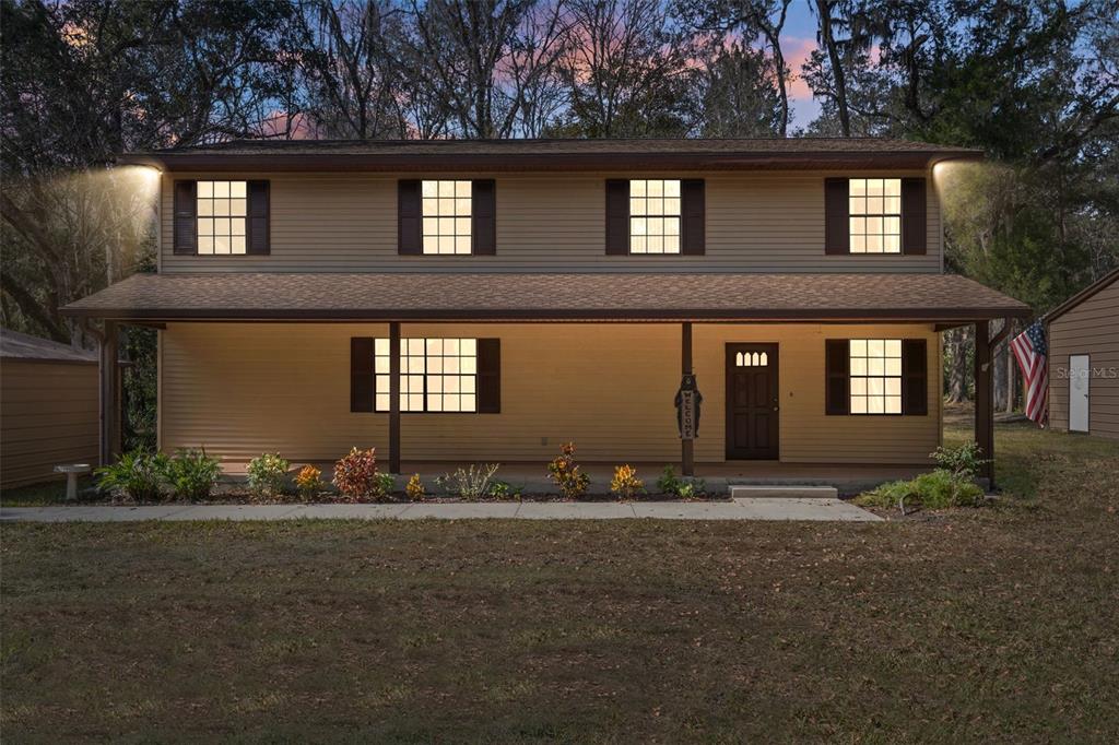 A two-story house with tan siding, a covered front porch, and dark shutters at dusk — 12047 TIMBER LANE, BROOKSVILLE, FL