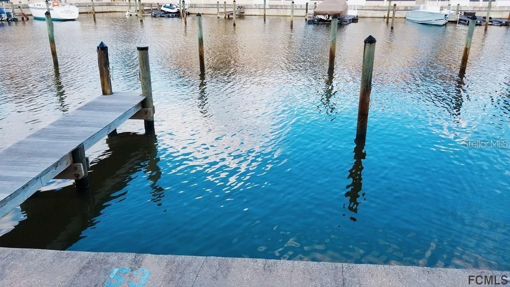 A wooden dock extends into a canal with several mooring pilings and boats in the background — 53 MARINA COVE UNIT B, PALM COAST, FL