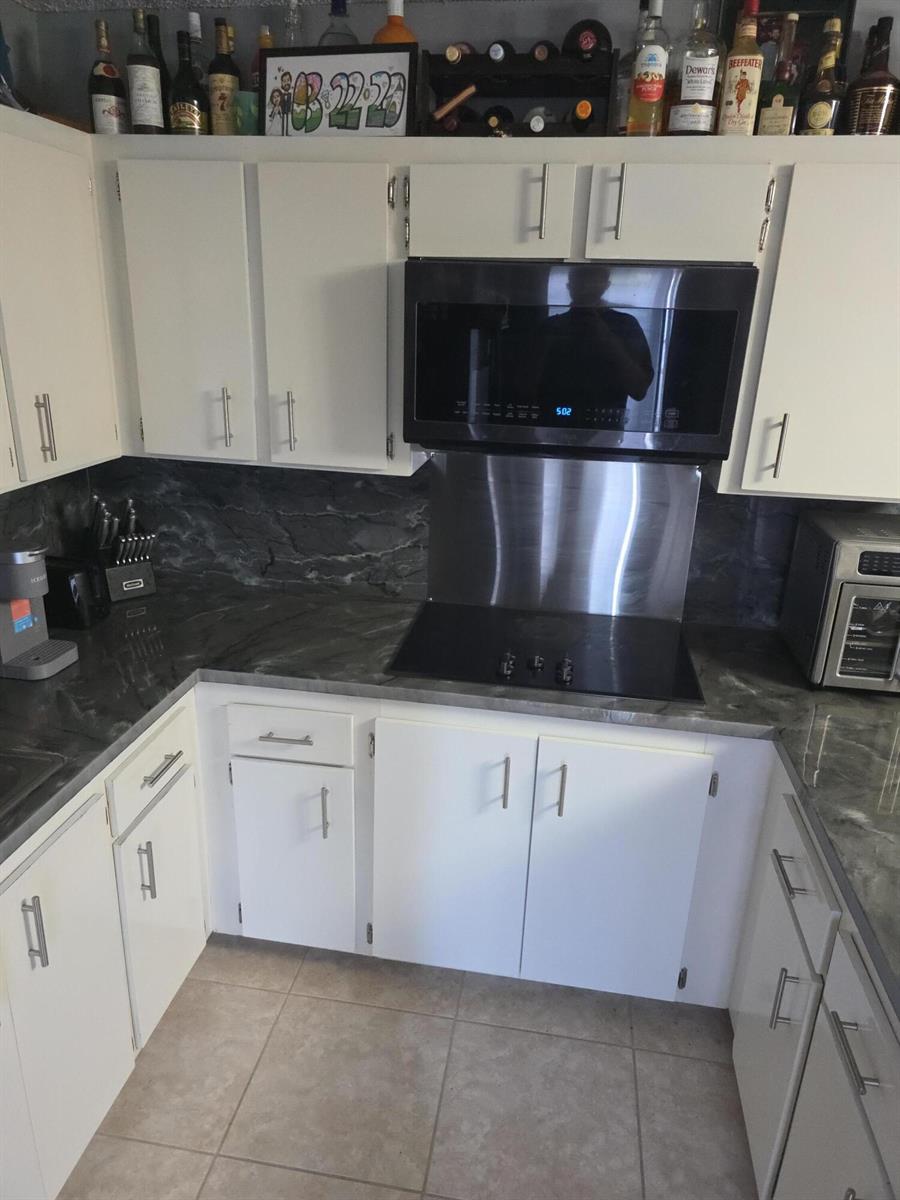 A kitchen features white cabinets, dark marble-patterned countertops, a stainless steel backsplash, and a microwave — 2164 White Pine Circle # B, FL 33415, FL