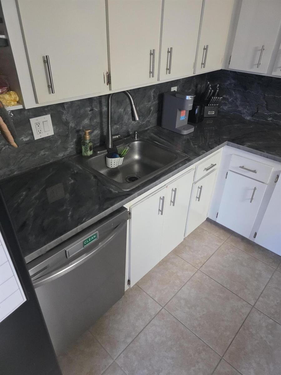 A kitchen features white cabinets, a dark marble-patterned countertop, and a stainless steel dishwasher — 2164 White Pine Circle # B, FL 33415, FL