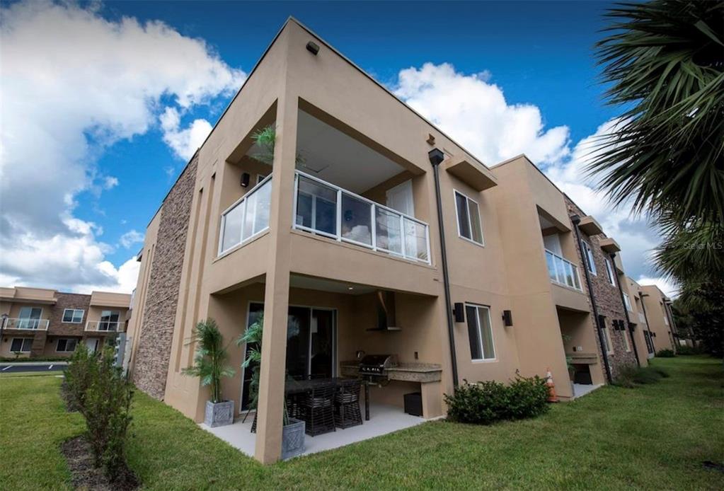 A two-story tan stucco building features a ground-level patio with a grill and upper balcony — 3229 BRASILIA AVENUE, KISSIMMEE, FL