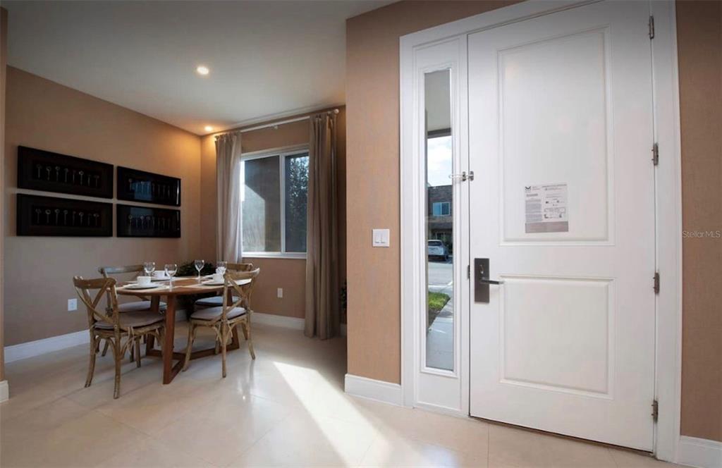 A dining area with a round table and chairs sits beside a white front door — 3229 BRASILIA AVENUE, KISSIMMEE, FL