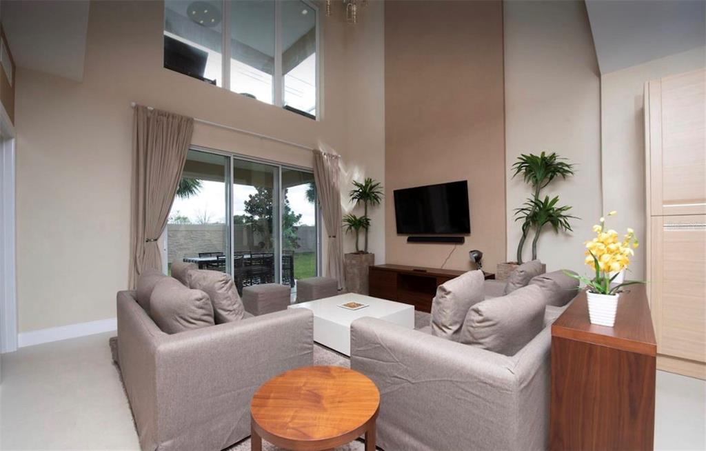 A living room features high ceilings, large windows, a wall-mounted television, and neutral furniture — 3229 BRASILIA AVENUE, KISSIMMEE, FL