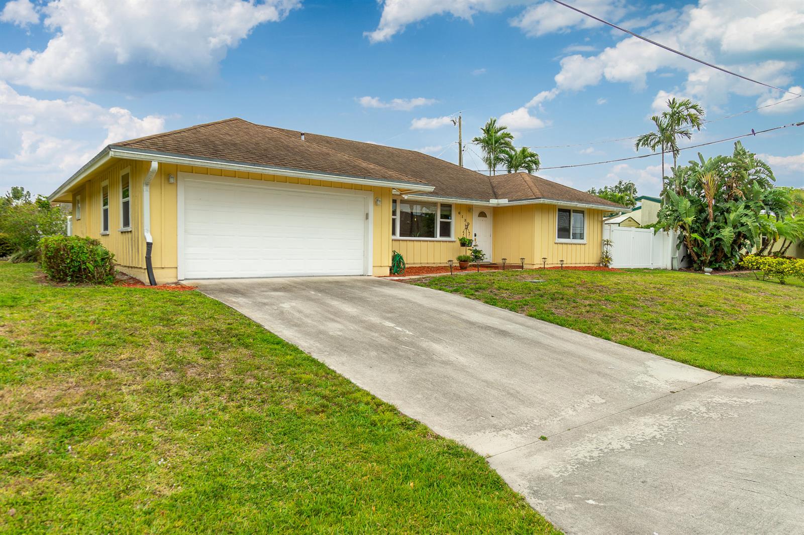 A yellow, single-story house with a white garage door and a concrete driveway — 6130 Francis Street, Jupiter FL 33458, JUPITER, FL