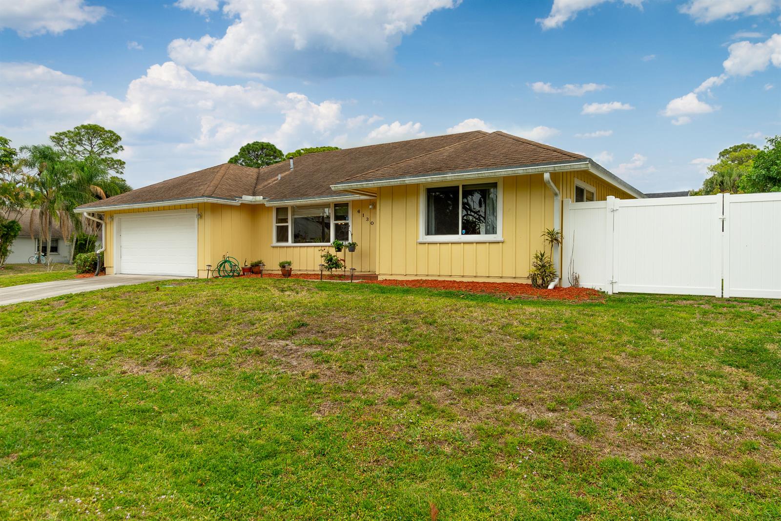 A yellow, single-story house features a white garage door, a brown roof, and white fencing — 6130 Francis Street, Jupiter FL 33458, JUPITER, FL