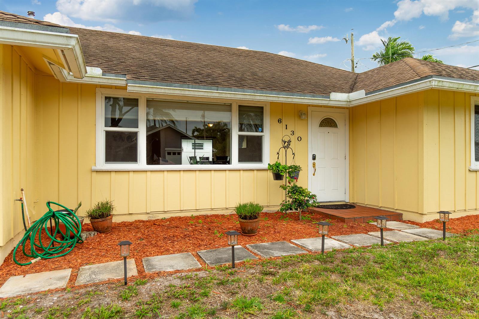 A yellow house exterior features a front door, a large window, and a landscaped yard — 6130 Francis Street, Jupiter FL 33458, JUPITER, FL