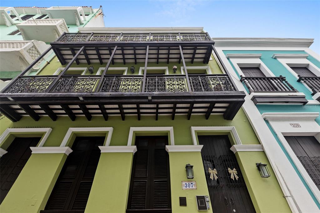 A low-angle view of a green building facade featuring a prominent black iron balcony — 307 SAN SEBASTIAN UNIT 2-B, SAN JUAN, PR