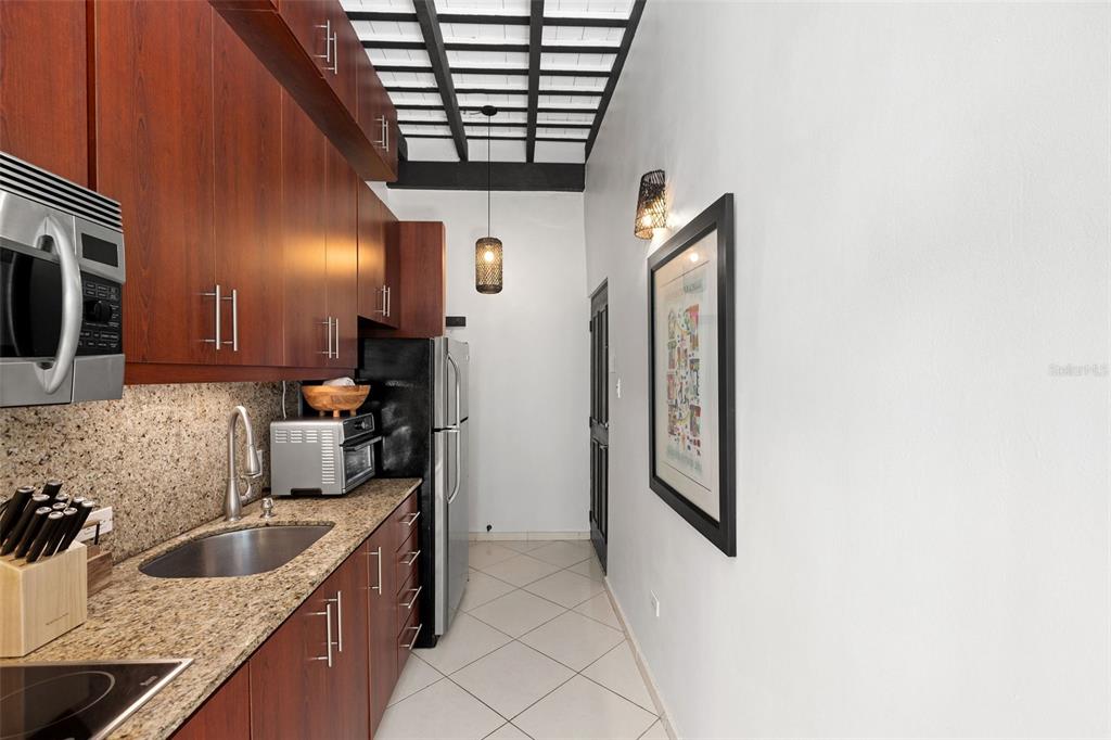 A galley kitchen features dark wood cabinets, granite countertops, stainless steel appliances, and tiled flooring — 307 SAN SEBASTIAN UNIT 2-B, SAN JUAN, PR