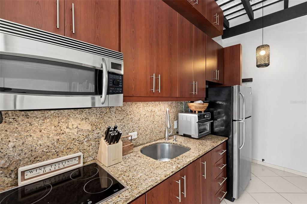A kitchen features wood cabinets, granite countertops, stainless steel appliances, and a black refrigerator — 307 SAN SEBASTIAN UNIT 2-B, SAN JUAN, PR