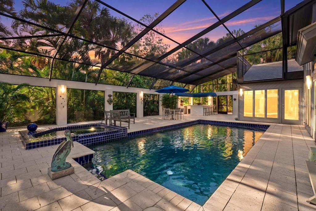 A screened-in pool area with a hot tub, outdoor bar, and patio furniture at sunset — 4891 PEREGRINE POINT E, SARASOTA, FL