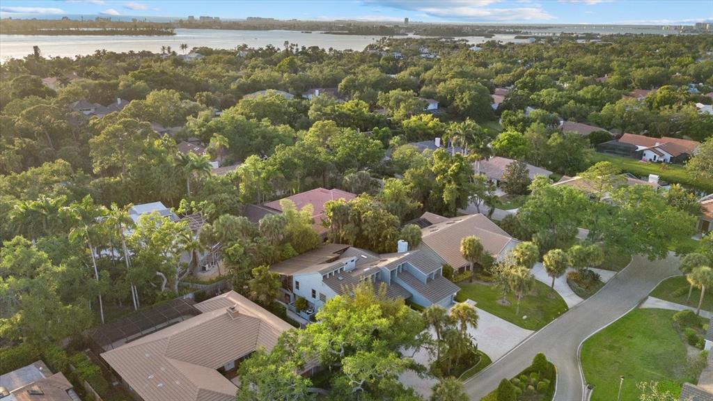 An aerial view shows several houses with tiled roofs nestled among dense green trees — 4891 PEREGRINE POINT E, SARASOTA, FL