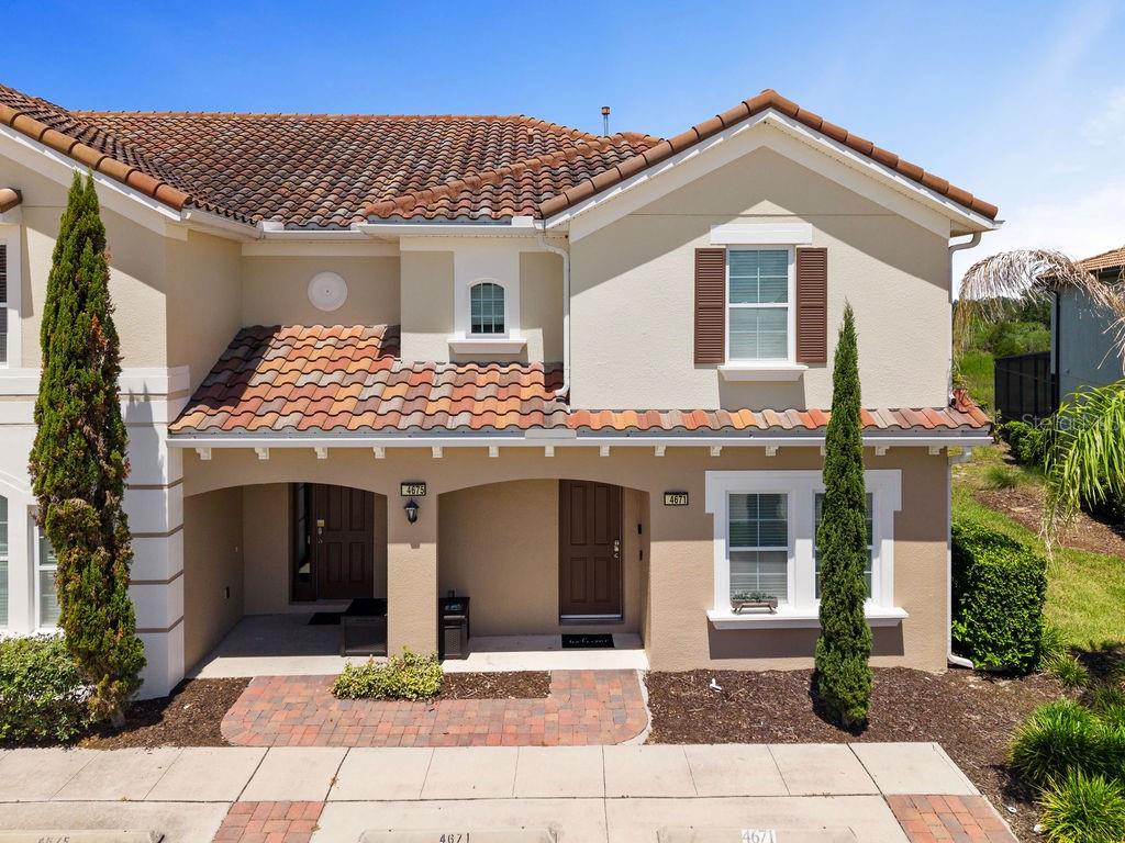 A two-story townhouse exterior features a tiled roof, beige stucco walls, and two front entrances — 4671 TERRASONESTA DRIVE, DAVENPORT, FL