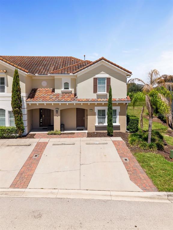 A two-story townhouse exterior features a tiled roof, stucco walls, and a concrete driveway — 4671 TERRASONESTA DRIVE, DAVENPORT, FL