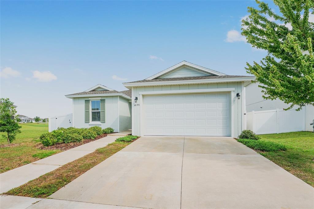 A light-colored single-story house features a two-car garage, a concrete driveway, and green landscaping — 6175 SW 74TH COURT, OCALA, FL