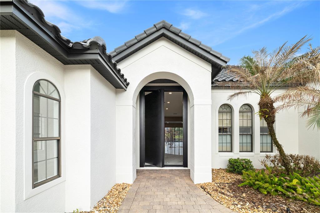 The exterior of a white stucco house features an arched entryway and a black door — 812 JOHNS POINT DRIVE, OAKLAND, FL