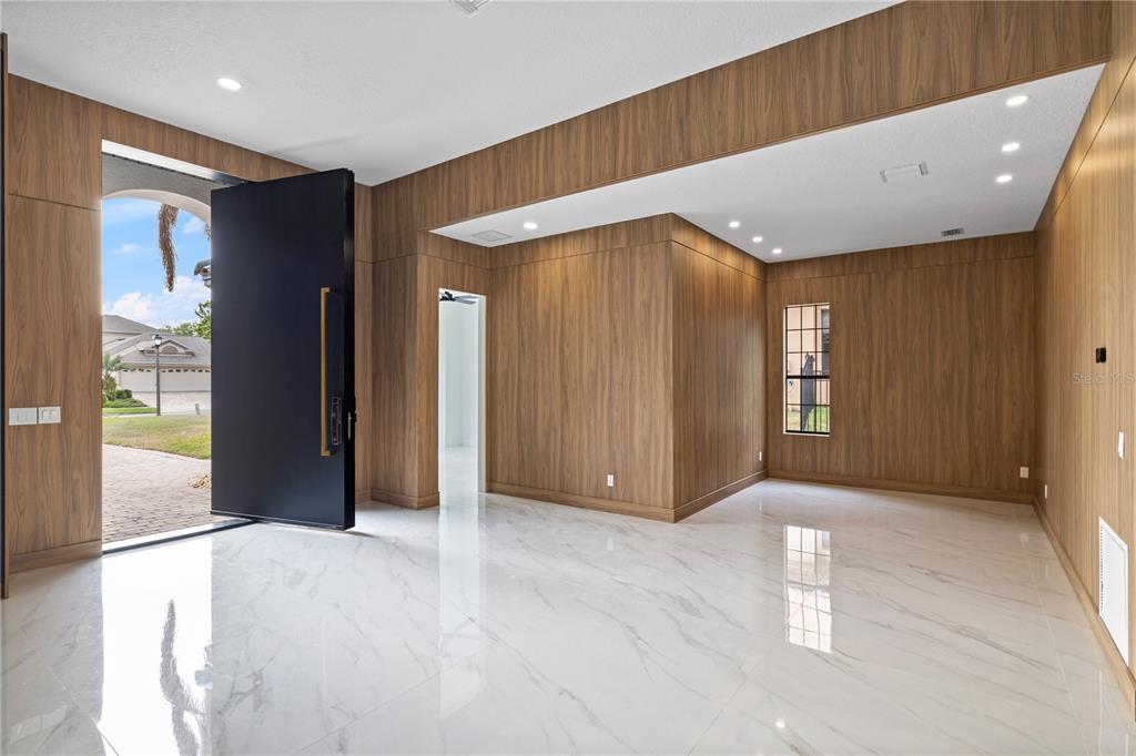 An entryway with wood-paneled walls, a large black pivot door, and white marble flooring — 812 JOHNS POINT DRIVE, OAKLAND, FL