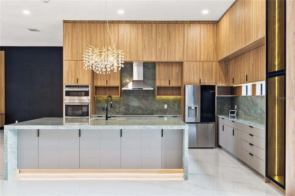 A modern kitchen features wood-toned upper cabinets, gray lower cabinetry, and a marble-topped island — 812 JOHNS POINT DRIVE, OAKLAND, FL