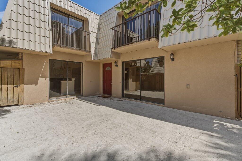 A beige two-story townhouse exterior features a concrete patio, a red door, and balconies — 5701 57th Way, West Palm Beach FL 33409, WEST PALM BEACH, FL