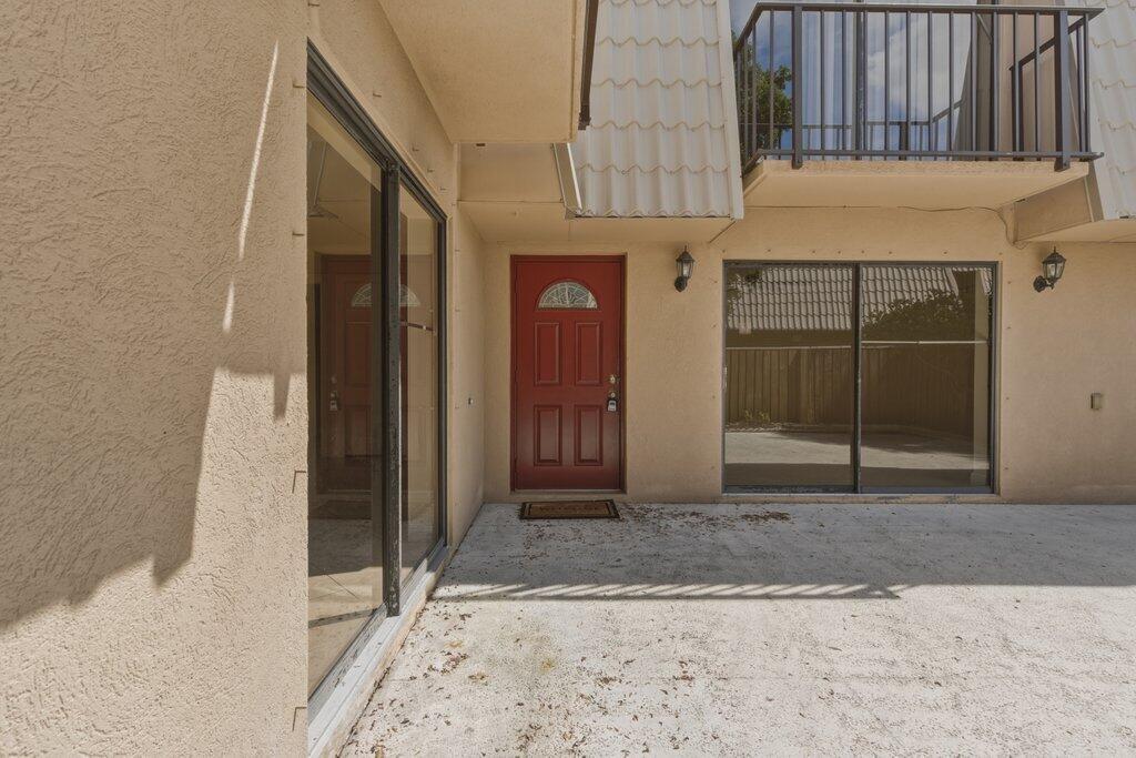 A red front door sits between two sliding glass doors on a concrete patio — 5701 57th Way, West Palm Beach FL 33409, WEST PALM BEACH, FL