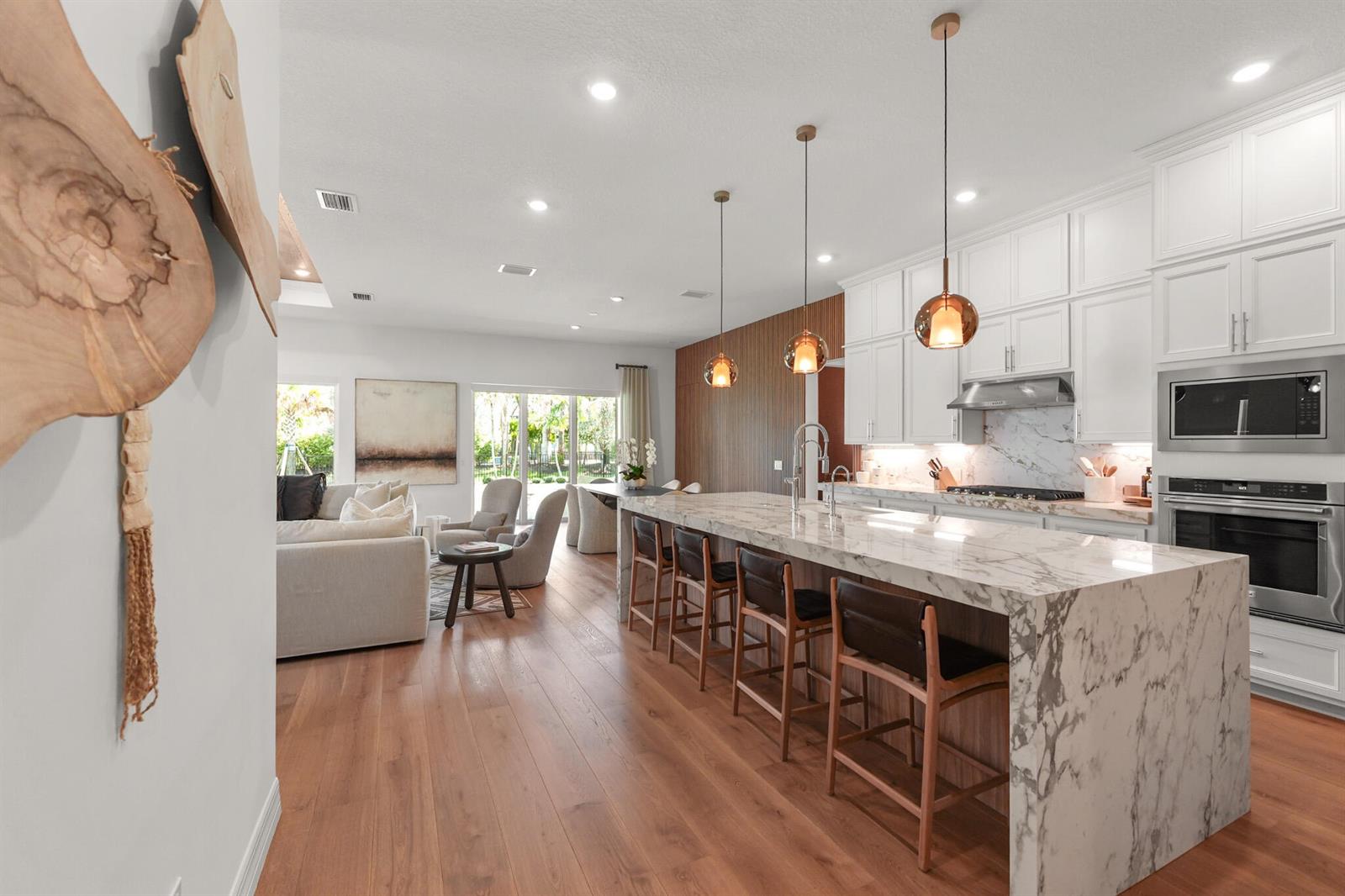 A modern kitchen features a large marble waterfall island with four leather bar stools — 10795 Stellar Circle, Palm Beach Gardens FL 33412, PALM BEACH GARDENS, FL