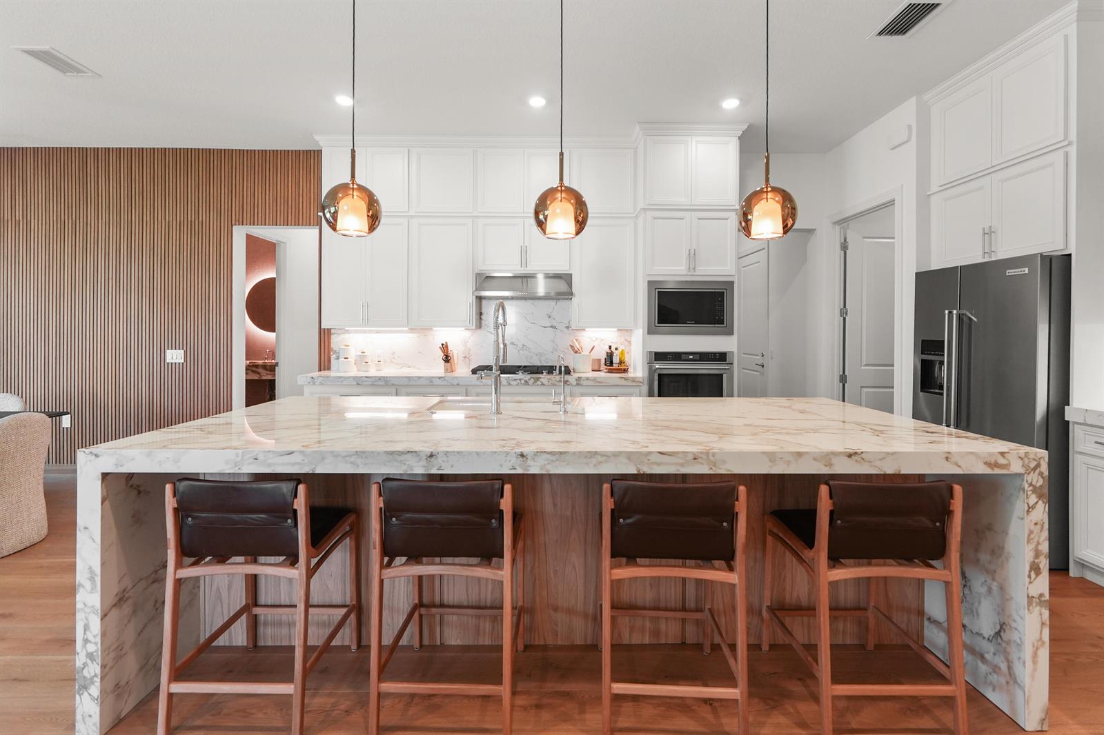 A modern kitchen features white cabinetry, marble countertops, a large island, and three pendant lights — 10795 Stellar Circle, Palm Beach Gardens FL 33412, PALM BEACH GARDENS, FL