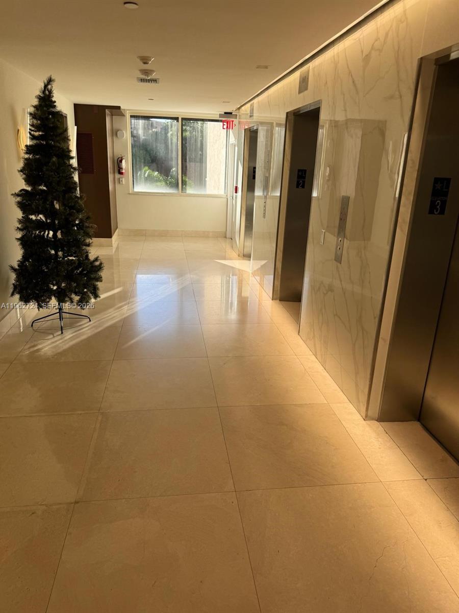 A brightly lit building hallway features light-colored tile flooring, two elevators, and a decorative tree — 540 Brickell Key Dr # 1505, Miami FL 33131, MIAMI, FL