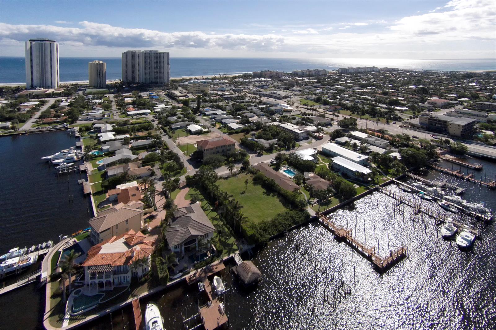 An aerial view shows a coastal neighborhood with houses, boat docks, and high-rise buildings nearby — 2715 Lake Drive, Riviera Beach FL 33404, RIVIERA BEACH, FL