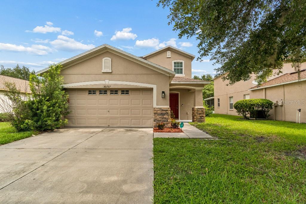 A two-story suburban house with a tan stucco exterior, stone accents, and a two-car garage — 30737 WHITE BIRD AVENUE, WESLEY CHAPEL, FL