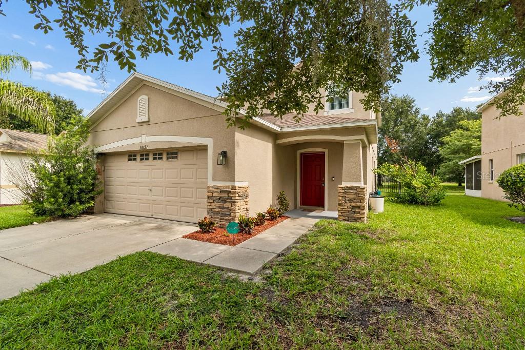A tan two-story house with a stone-accented entryway, red front door, and attached garage — 30737 WHITE BIRD AVENUE, WESLEY CHAPEL, FL