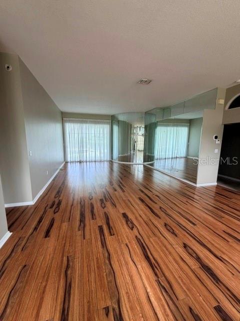 An empty room features wood-look flooring, a curved mirrored wall, and floor-to-ceiling window treatments — 16525 MAJESTIC COURT, CLERMONT, FL