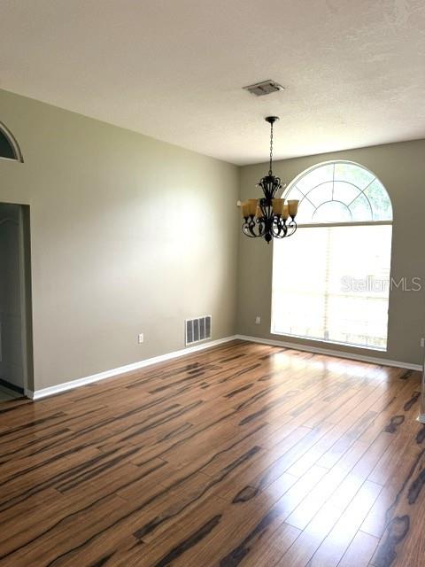 An empty room features wood-look flooring, a chandelier, and a large arched window — 16525 MAJESTIC COURT, CLERMONT, FL
