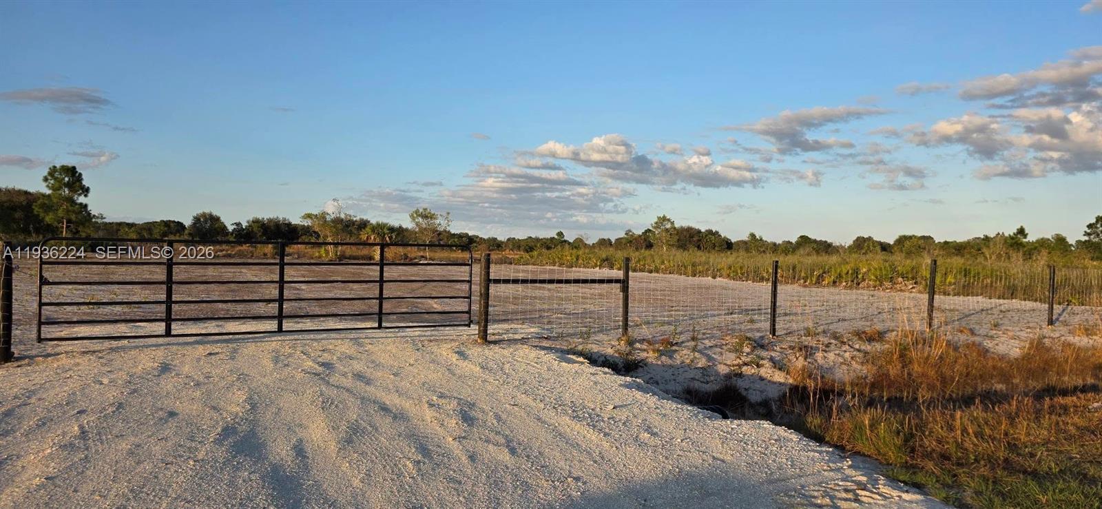A metal gate opens onto a sandy, fenced-in plot of land under a blue sky — 17385 NW 314 st, Okeechobee FL 34972, OKEECHOBEE, FL
