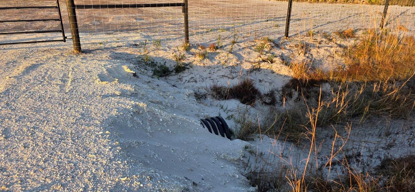 A black corrugated drainage pipe is partially buried in a sandy embankment near a fence — 17385 NW 314 st, Okeechobee FL 34972, OKEECHOBEE, FL